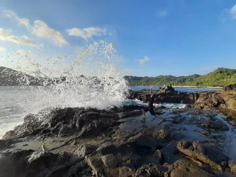 A man on a rock short time before getting wet from a big wave Foto stock