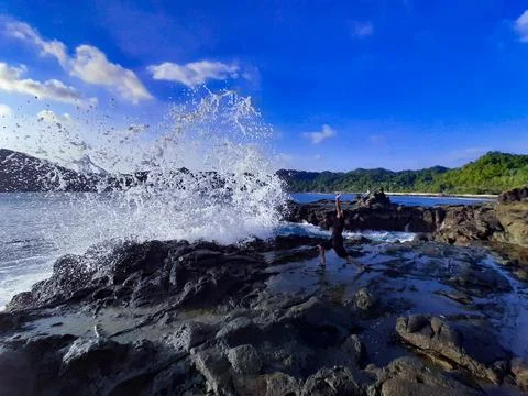 A man on a rock short time before getting wet from a big wave Foto stock