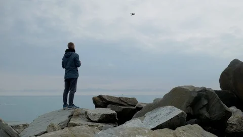Man in rocks coast catch the drone in hand Stock Footage 104869236