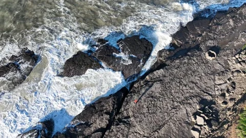 Man on rocks looking at waves incoming aerial view Wexford Ireland epic Stock Footage 330854338