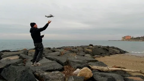 A man on a rocky beach lands a drone on his hand Stock Footage 86053751