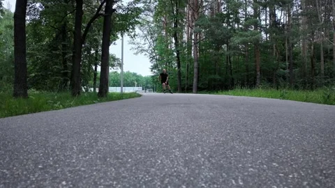 Man roller skates fast on a path in a forest during the day Stock Footage 338307017