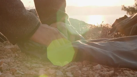 Man rolling his sleeping bag on a cliff above the ocean in sunlight dawn Stock Footage 121804812