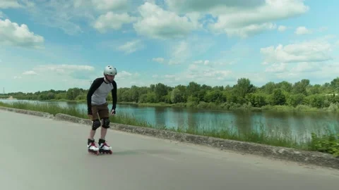Man rolling on inline skates on a sunny summer day wearing knee pads helmet Stock Footage 132798780