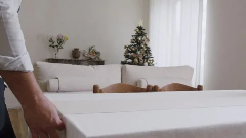 A Man is Rolling a Table Runner Over the Dining Table in Preparation for the Stock Footage 296326193
