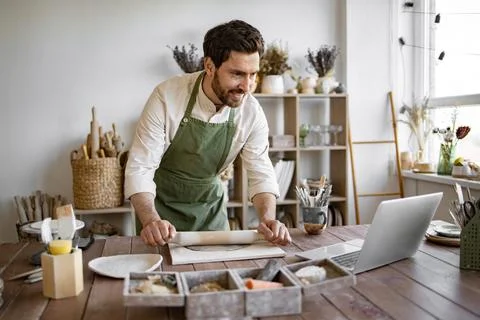 Man rolls clay with rolling pin in a bright and cozy pottery studio. Stock Photos