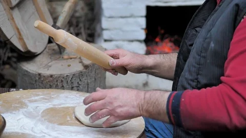 Man rolls dough with a rolling pin for baking flatbread in the medieval oven. Video stock 125504922