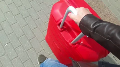A man rolls a large red suitcase on the sidewalk on wheels Stock Footage 154739247