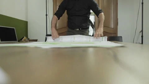 Man rolls up a map from a table Vídeos de archivo 133495324