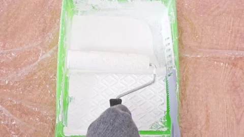 A man rolls white acrylic paint into paint tray on a foam roller. Painting the Stock Footage 200649622