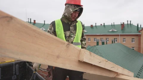 Man on rooftop actively positions large wooden beam Stock Footage 311105603
