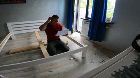 The man in the room assembles the bed according to the instructions Stock Footage 197349790