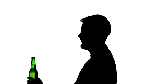 Man in the room sits opens and drinks from the bottle. Side view. Silhouette 스톡 동영상 101772892