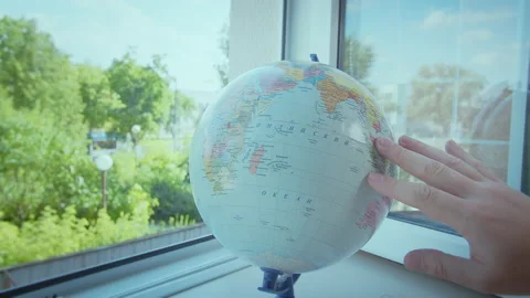 The man rotates the globe, which stands on the windowsill by the open window Stock Footage 168912653