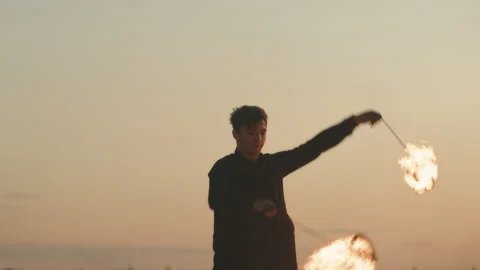 Man Rotating Burning Objects during Fire Show at Sunset Stock Footage 249588995