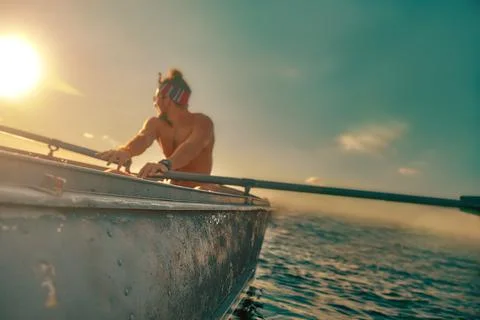 A man is rowing on the oars along the riverbed at sunset. Sunset sun, view from Stock-Fotos