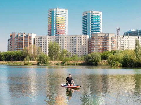 Man rowing on paddle surf board SUP in the lake in the city among the houses Stock-Fotos