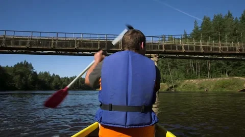 Man Rows a Canoe on the River, Paddles Beneath the Bridge Stock Footage 285144221