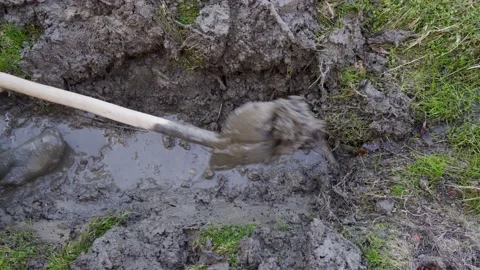 A man in rubber boots clears a channel for water flow with a shovel. Stock Footage 172531143