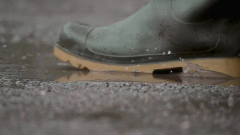 Man in rubber boots jumping into a puddle. Water splashes in slow motion Stock Footage 310169573