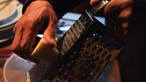 Man is rubbing parmesan into a plastic bawl on a wooden table. Hands rub ch.. Video stock 277456894