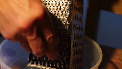 Man is rubbing parmesan into a plastic bawl on a wooden table. Hands rub ch.. Video stock 277456910