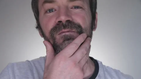 The man rubs his gray beard and decides to paint it with black mascara Stock Footage 132024552