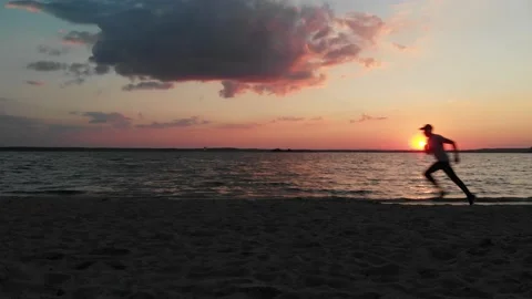 Man running against the background of sunset fast along the sandy shore of the Stock Footage 222305359