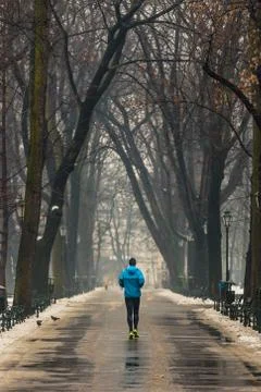 Man running along path surrounded by trees, in winter, using blue sports jack Stock Photos