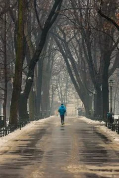 Man running along path surrounded by trees, in winter, using blue sports jack Stock Photos