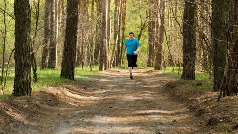 The man is running around the forest trail. A fat person jogging in park. Stock-Footage 89156818
