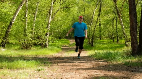 The man is running around the forest trail. A fat person jogging in park. Stock-Footage 89156991