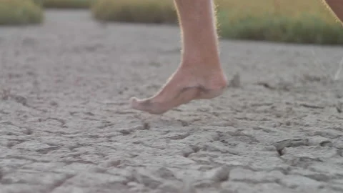 Man running barefoot on bottom of dried lake or cracked soil ground. Side view Stock Footage 196822218