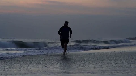 Man running on the beach and splashing water, steadycam shot, slow motion shot a Video stock 82452816