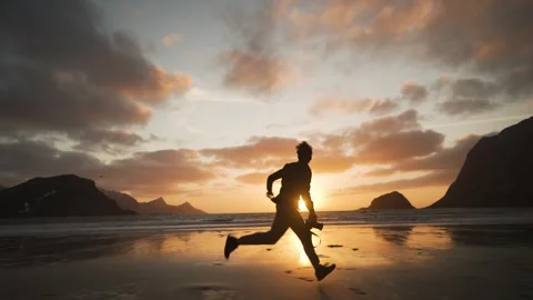 Man running on a beach at the sunset holding a camera Stockbeeldmateriaal 304582070