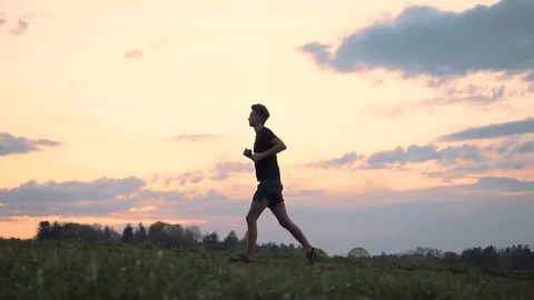 Man running on grass meadow during colourful sunset, slow motion Stock Footage 129615053