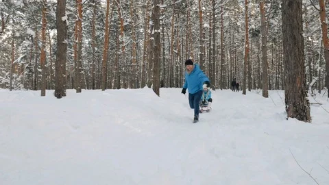 Man running in park at winter day and pulling his laughing girlfriend on sledge Stock Footage 86561083
