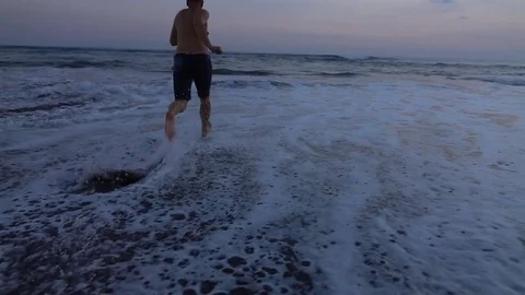 Man running to the sea, slow motion shot at 240fps, steadycam shot  Video stock 80417591