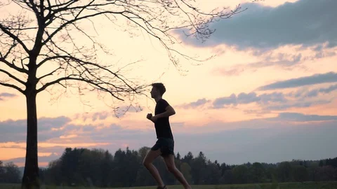 Man running through trees and bench during colourful sunset, slow motion Stock Footage 129615698