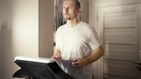 Man running on a treadmill at home. Middle-aged man in a grey t-shirt exerc.. Stock Footage 332162190