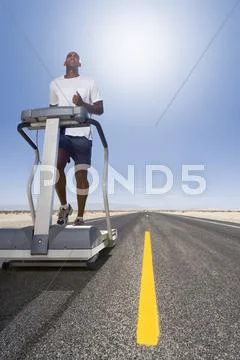 Man running on treadmill on remote desert road Stock Photos
