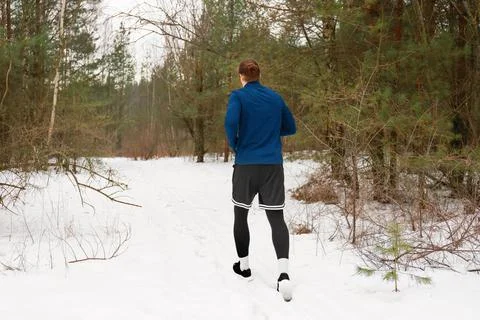 Man running in winter forest exercising on snow path Stock Photos