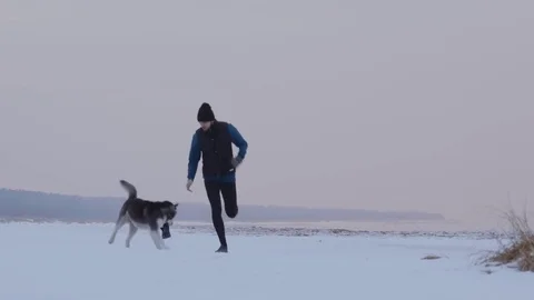 A man running in winter on a snowy beach with a dog 動画素材 85400007