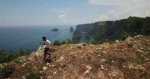Man Runs Along and Flips on Cliff to Reveal Ocean Drone Shot Stock Footage 106787934