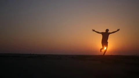 A man runs along the beach and is spinning with his hands up in the sunset. HD Stock Footage 80245585
