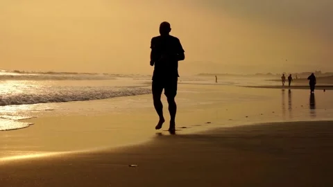 A man runs along the ocean at sunset, a young man trains on the shore of a Stock Footage 241769841