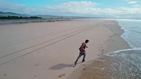 A man runs away from a wave by the ocean Stock Footage 231346239