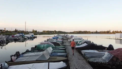 A man runs on the dock between boats, in a river bay. Triathlete Running Stock-Footage 142815030