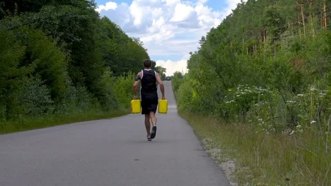 Man runs on the road with two yellow jerrycans Stock Footage 80436069