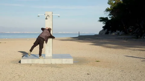 Man runs to shower rack on beach and turns off water. Waste of water, person Stock Footage 231283389